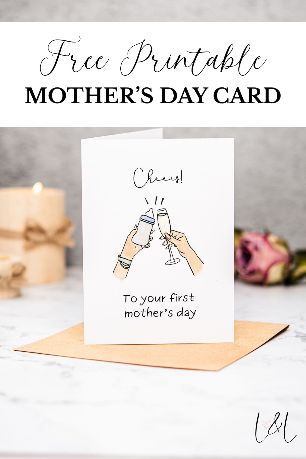 A First Mothers Day Card stands on an envelope, showing two hands clinking a baby bottle and a champagne glass with the words Cheers! To your first mothers day. A candle and pink flower add a warm touch in the background.