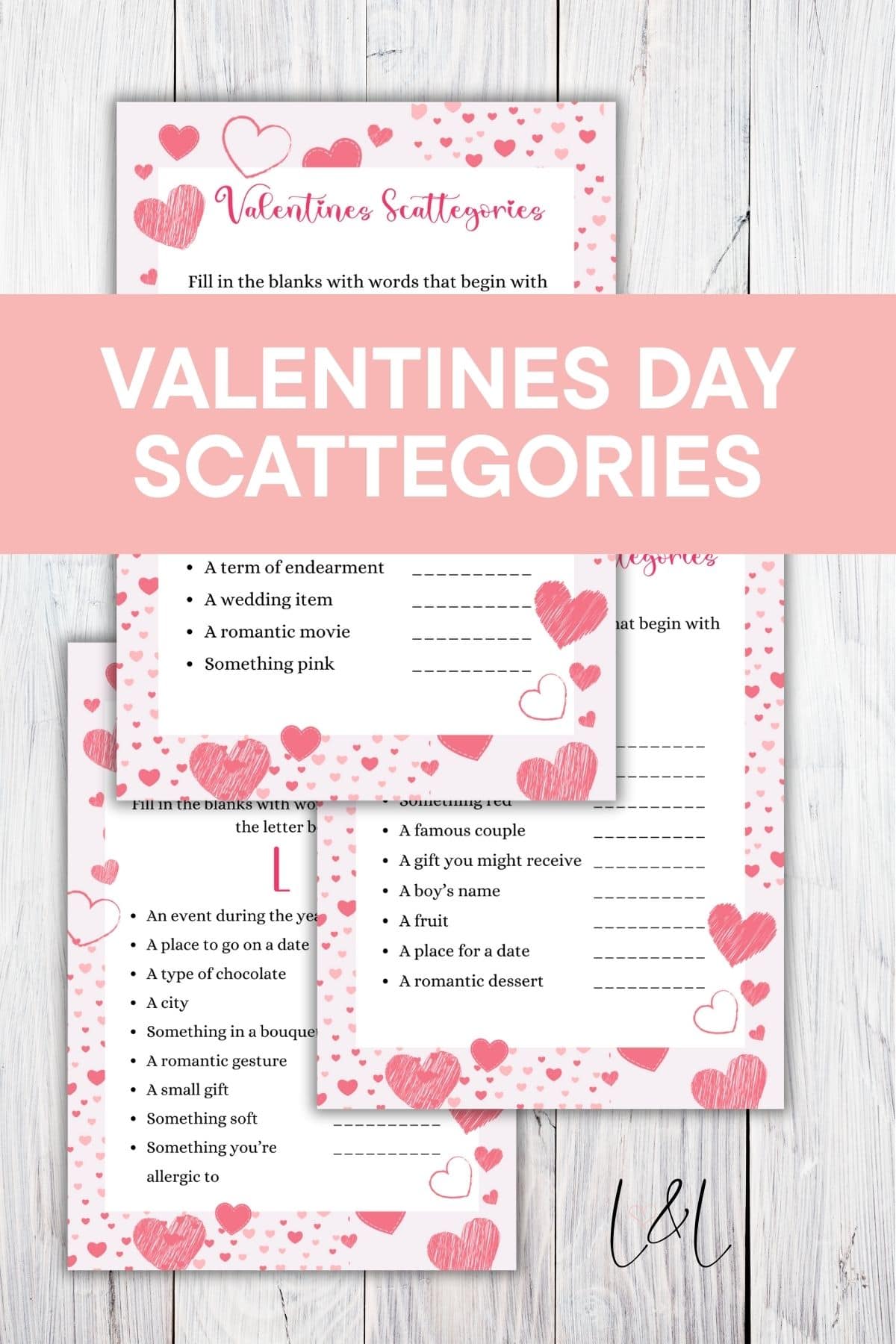 A stack of Valentines Day Scattergories game cards with pink hearts and dotted borders on a wood background. A pink banner across the middle reads VALENTINES DAY SCATTEGORIES in white text.