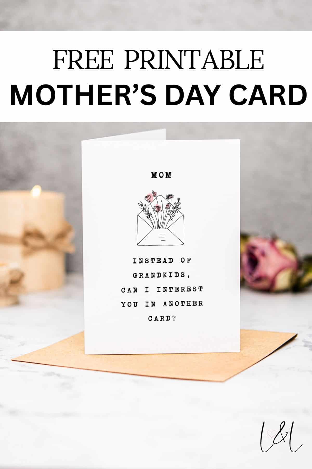 A printable Mother’s Day card stands on a marble surface. The card reads, “Mom, instead of grandkids, can I interest you in another card?” with a small floral illustration above the text. A rose and candle are in the background.