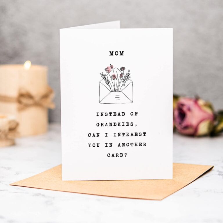 A Free Funny Mothers Day Card on a brown envelope reads, “MOM. Instead of grandkids, can I interest you in another card?” with a flower-filled envelope illustration. A lit candle and rose decorate the background.