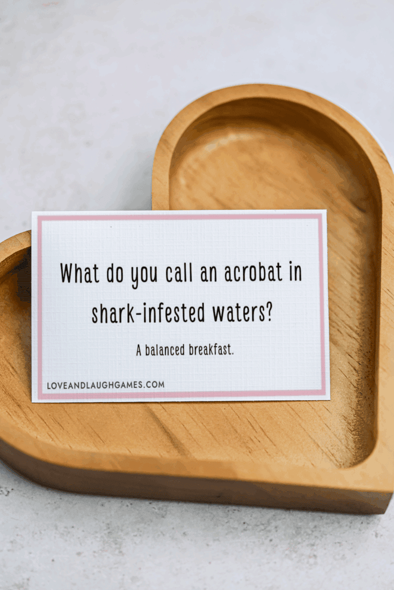 A card on a wooden heart-shaped tray reads: What do you call an acrobat in shark-infested waters? A balanced breakfast. Perfect for fans of Acrobat Jokes!.