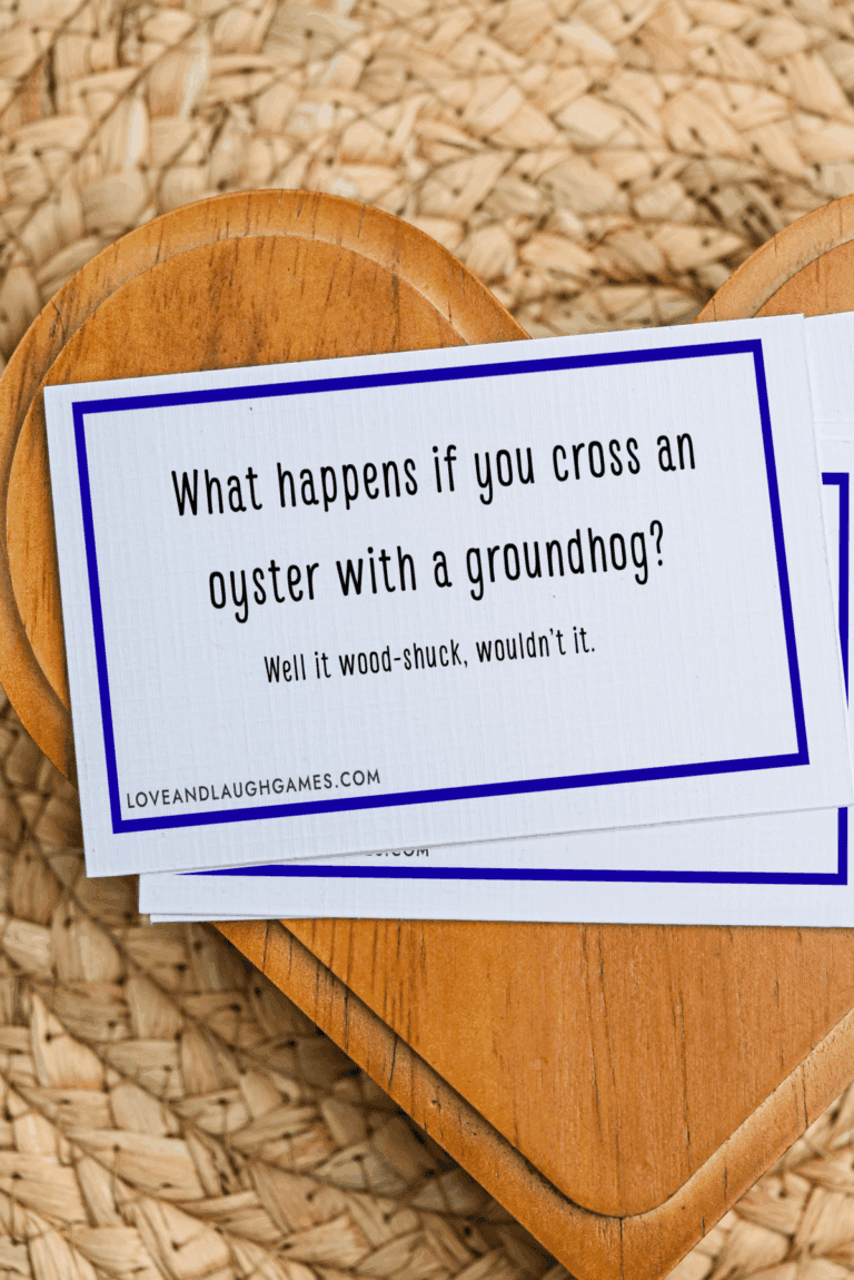 A card reads: What happens if you cross an oyster with a groundhog? Well it wood-shuck, wouldn’t it. Perfect for fans of oyster jokes, the card rests on a wooden heart atop a woven mat.
