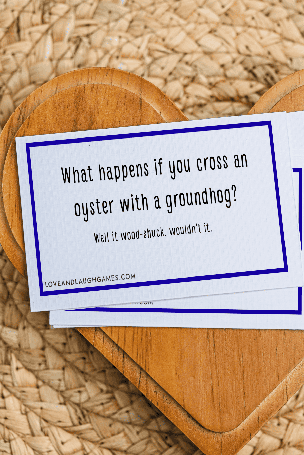 A card reads: What happens if you cross an oyster with a groundhog? Well it wood-shuck, wouldn’t it. Perfect for fans of oyster jokes, the card rests on a wooden heart atop a woven mat.
