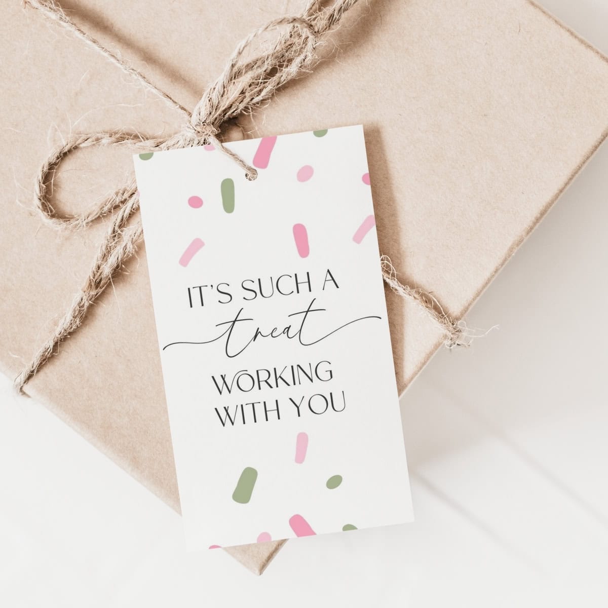 A brown gift box tied with twine features a white Employee Appreciation Gift Tag decorated with pink and green confetti. The tag reads, It's such a treat working with you.