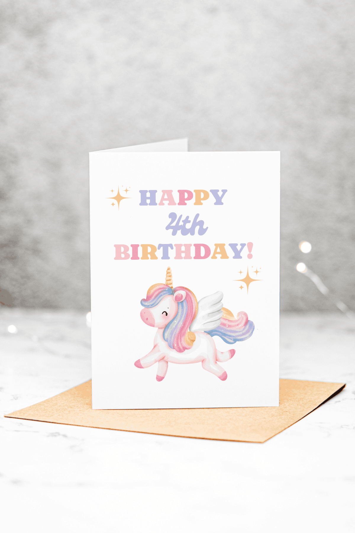A Unicorn 4th Birthday Card featuring HAPPY 4th BIRTHDAY! in colorful letters above an illustrated unicorn with rainbow hair and wings, placed on a brown envelope against a light background.