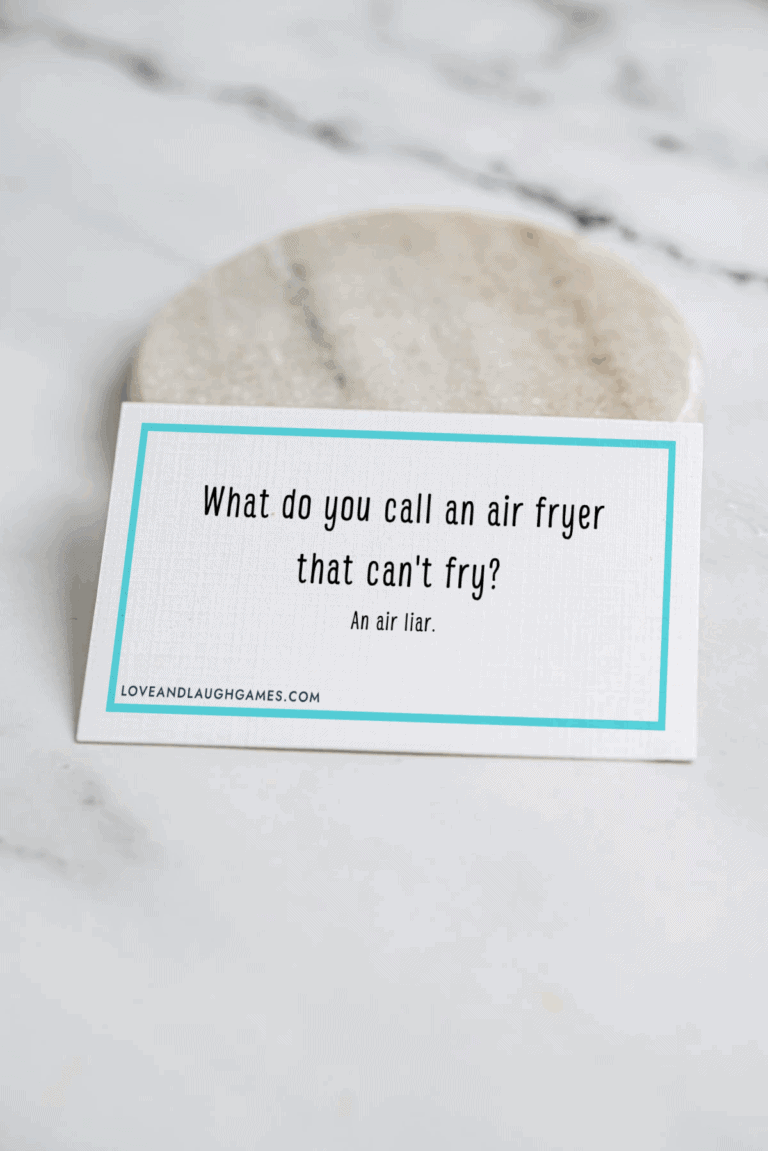 A card on a marble surface reads: What do you call an air fryer that cant fry? An air liar. The card has a blue border and the website loveandlaughgames.com at the bottom.