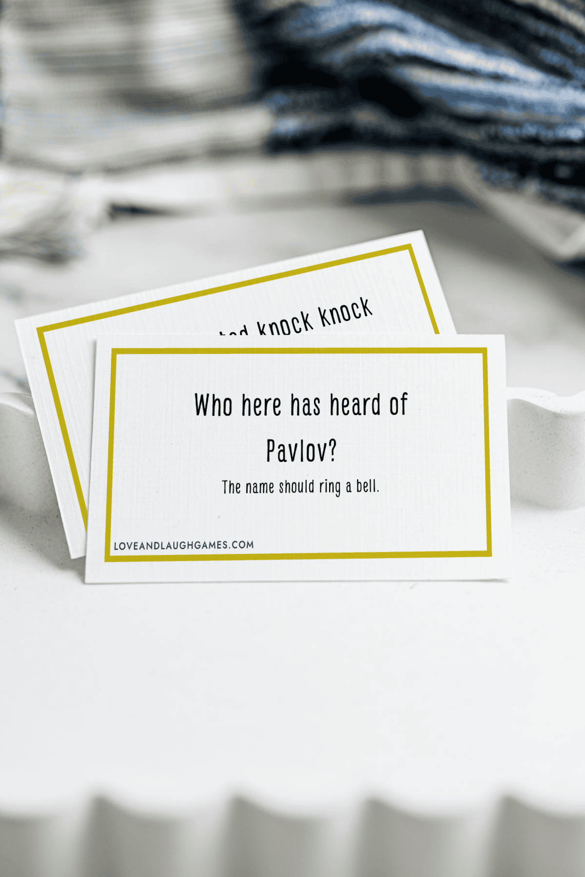 A card reads, Who here has heard of Pavlov? The name should ring a bell. Another card is partially visible behind it. Both cards are on a white surface with folded fabric in the background.