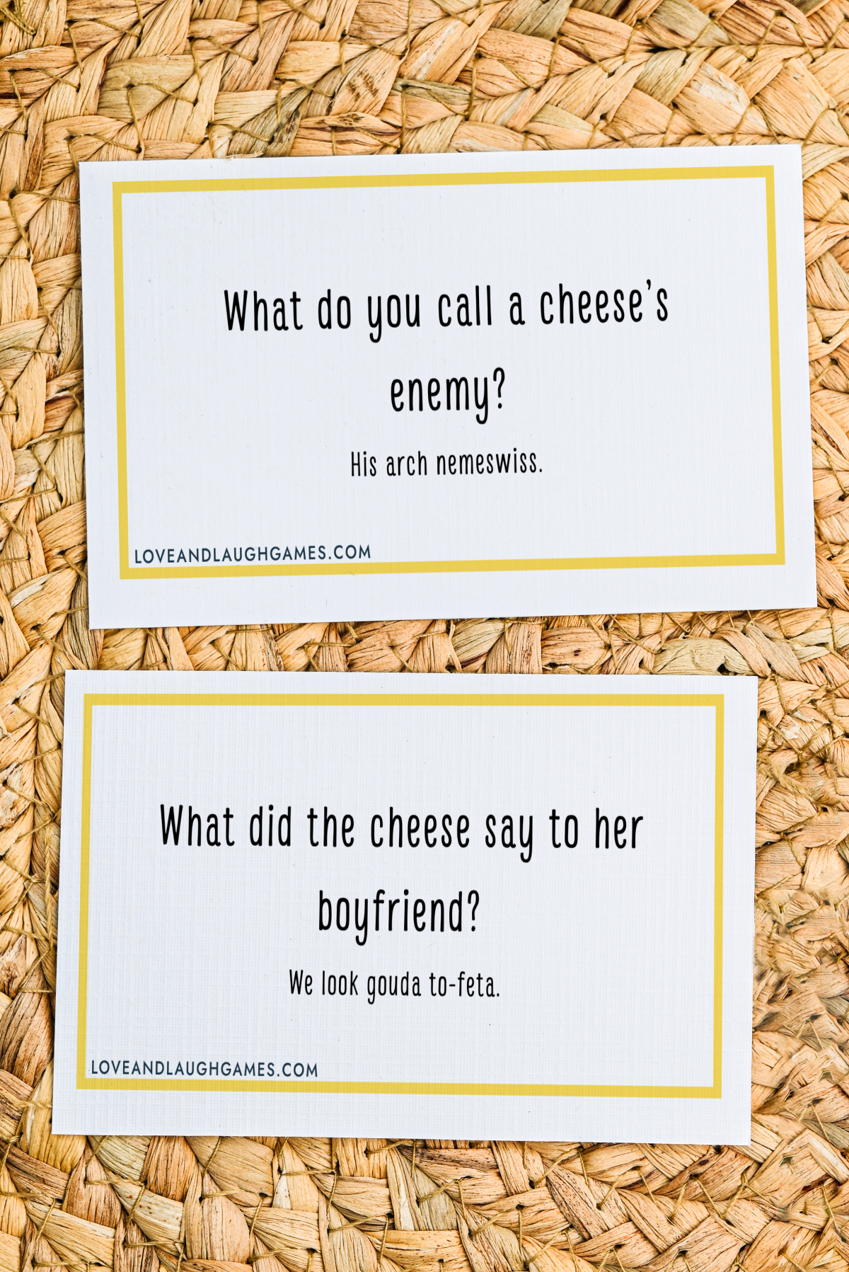 Two cards with cheese jokes on a woven surface. The first card: What do you call a cheese’s enemy? His arch nemeswiss. The second card: What did the cheese say to her boyfriend? We look gouda to-feta.