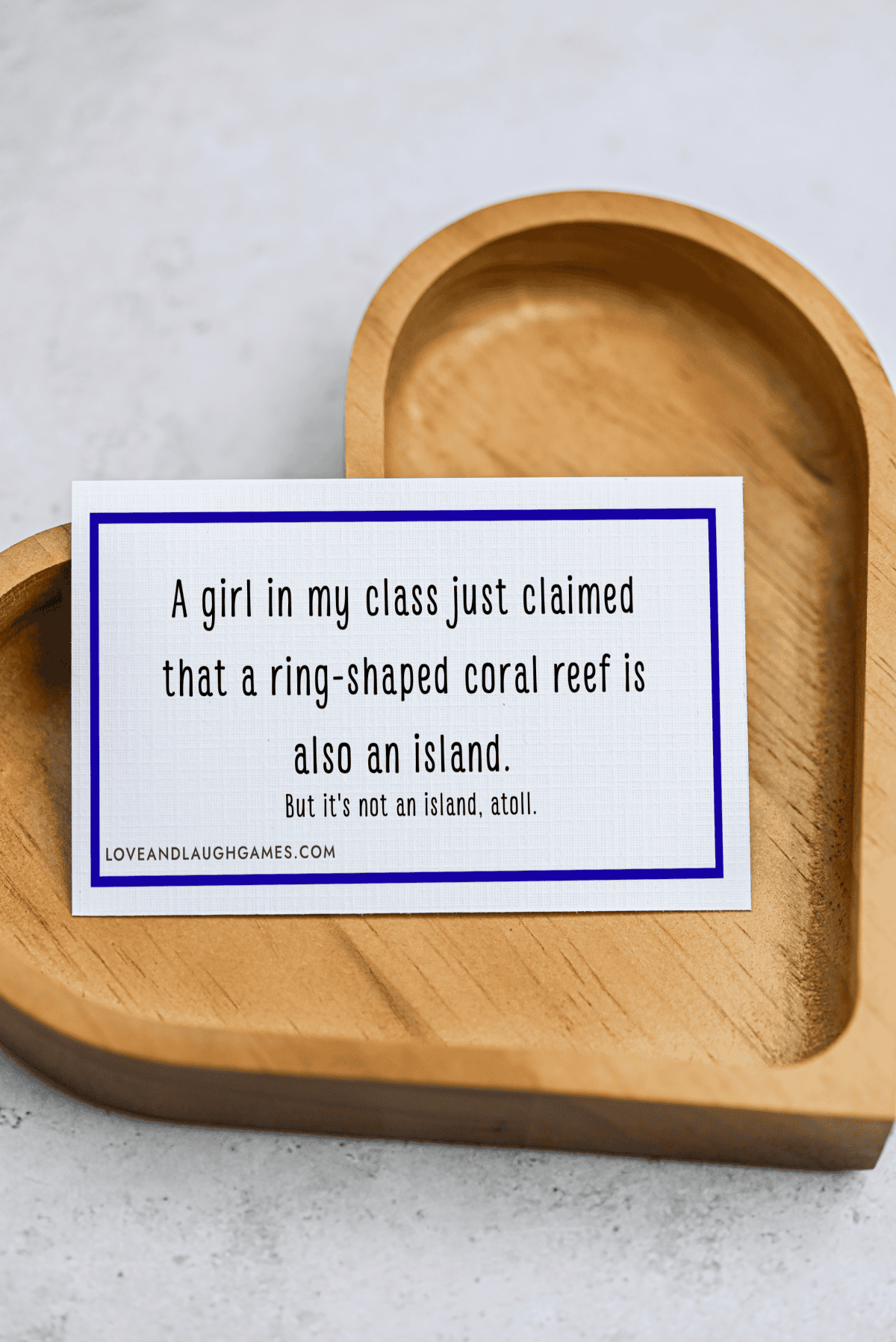 A card on a wooden heart tray reads: A girl in my class just claimed that a ring-shaped coral reef is also an island. But its not an island, atoll.