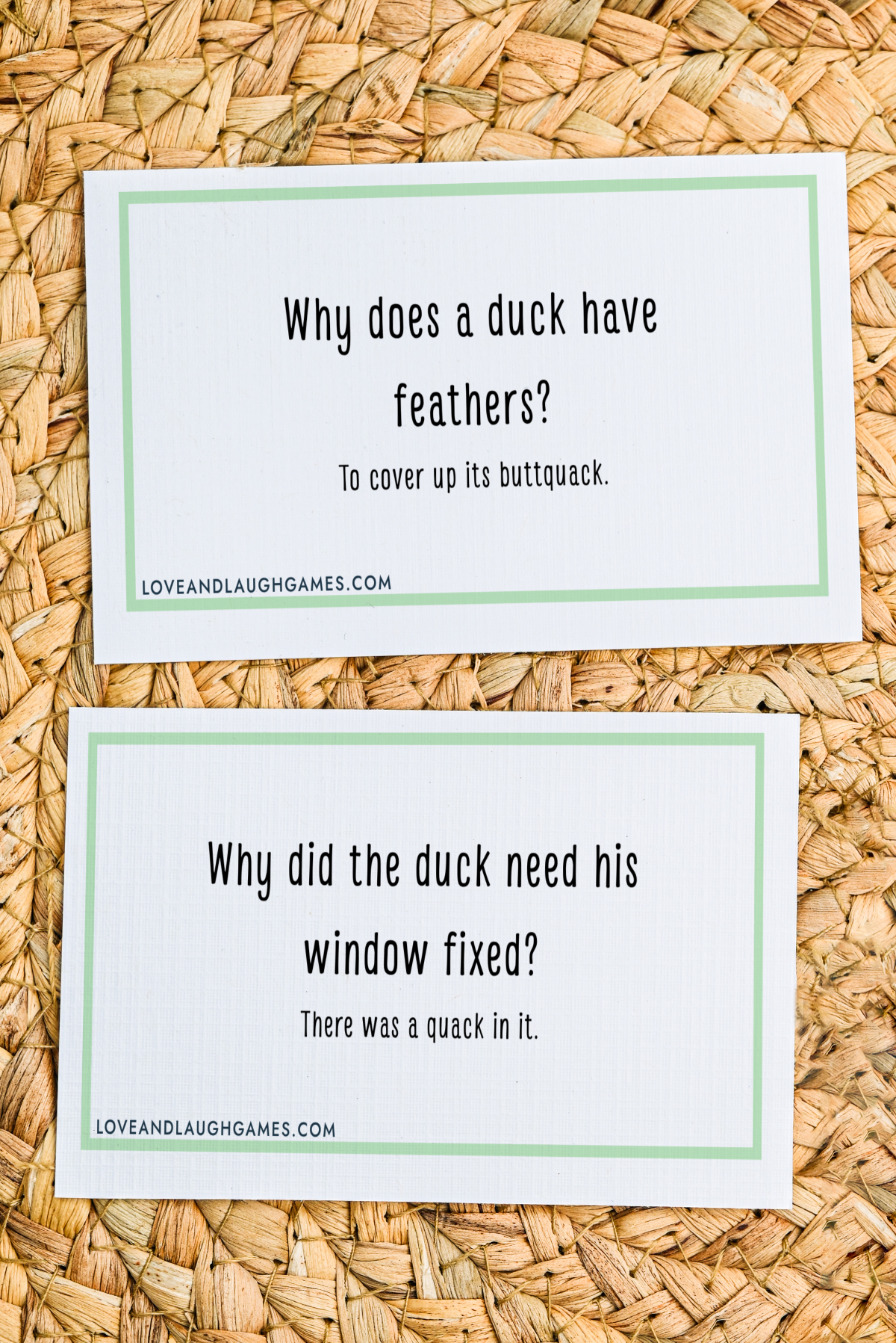 Two cards on a woven surface feature duck jokes. The first asks, Why does a duck have feathers? Answer: To cover up its buttquack. The second: Why did the duck need his window fixed? Answer: There was a quack in it.