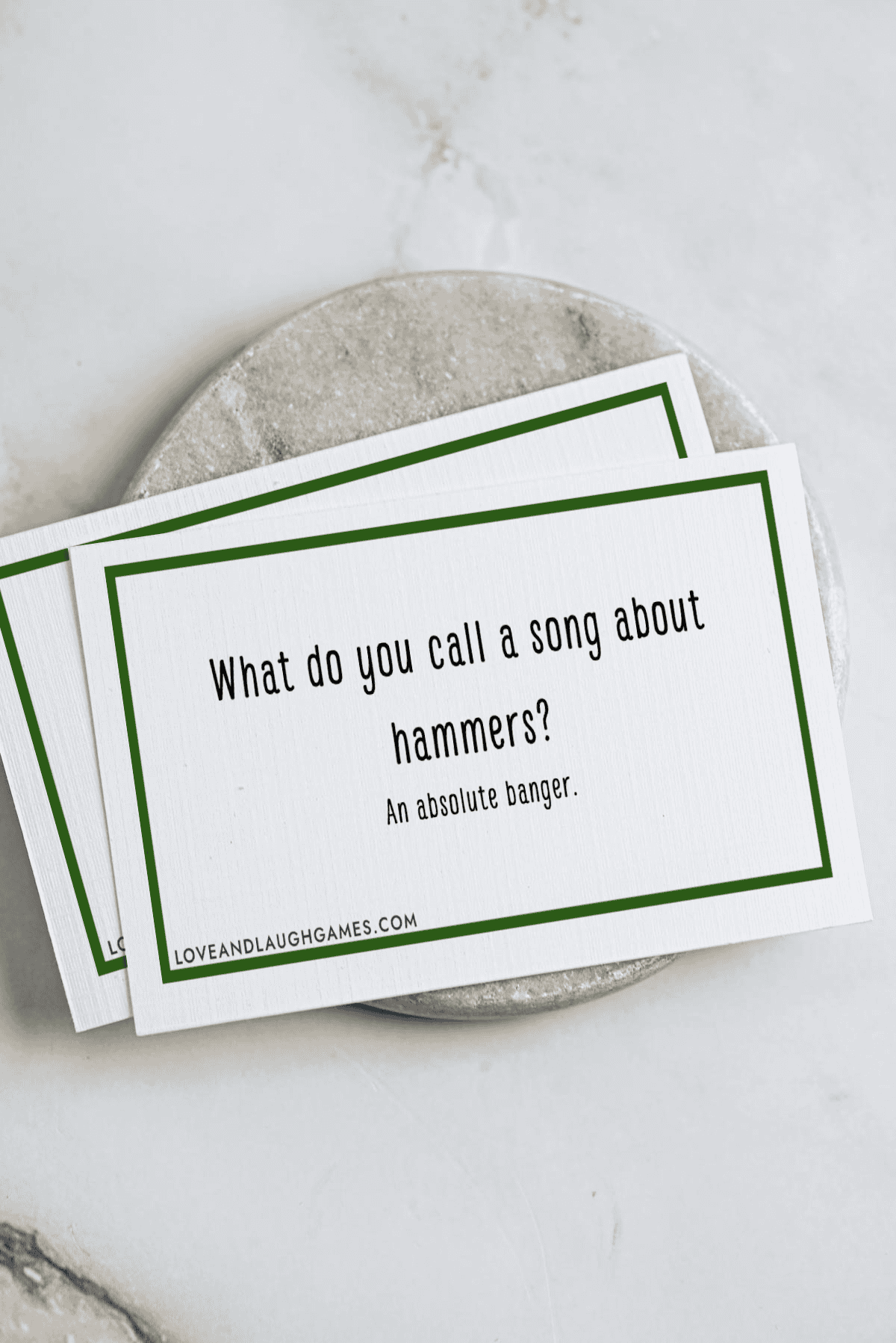 A card with the text: What do you call a song about hammers? An absolute banger. The card rests on a round marble surface atop a white background.