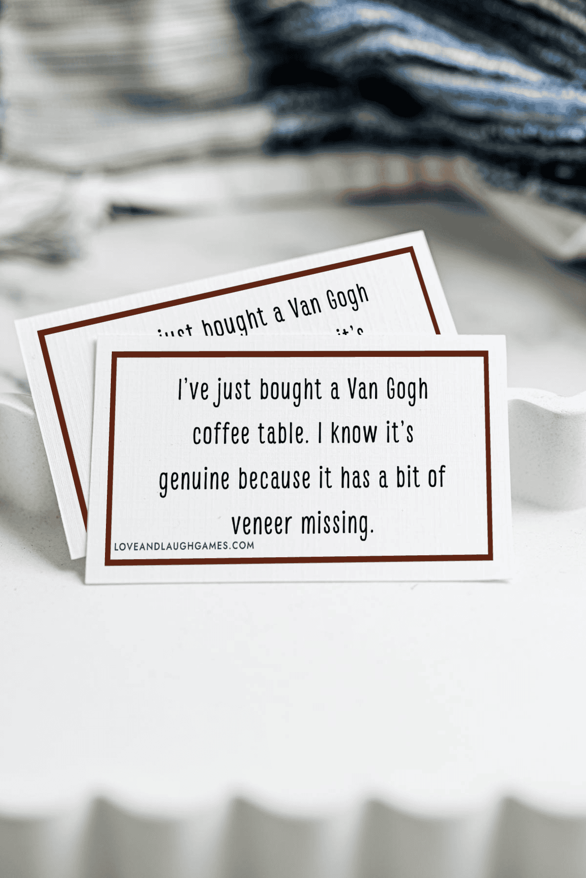 A card on a white tray reads: Ive just bought a Van Gogh coffee table. I know its genuine because it has a bit of veneer missing. Another similar card is partially visible behind it.
