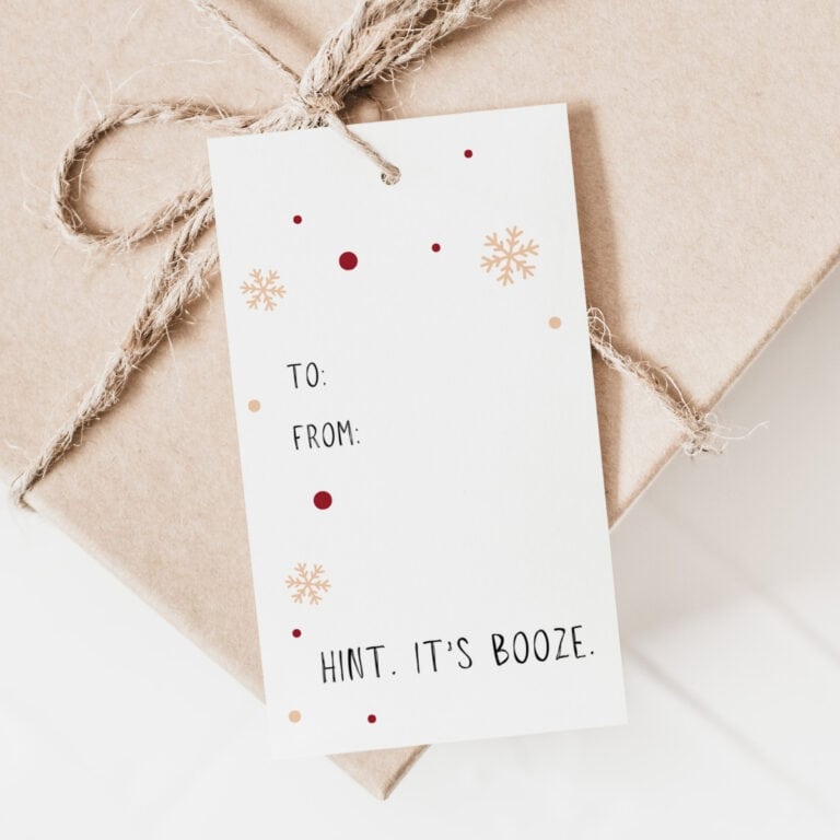 A kraft paper-wrapped gift tied with twine features festive Gift Tags that read, TO: FROM: HINT. ITS BOOZE., accented by small red dots and gold snowflakes decorating the card.
