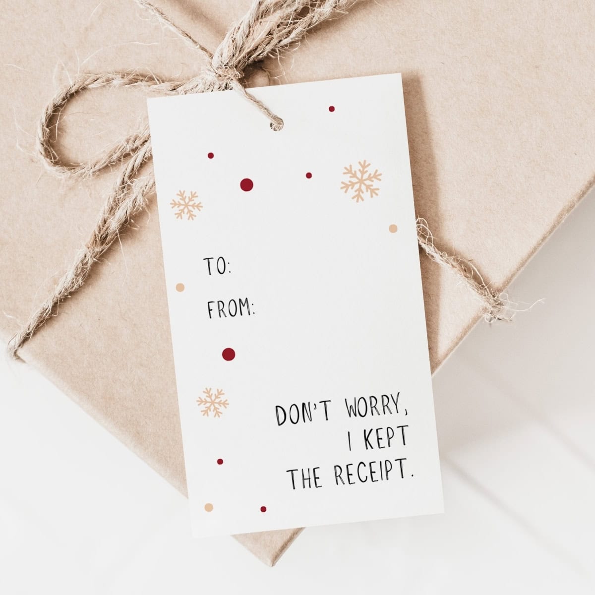 A brown gift box tied with twine features festive Gift Tags decorated with snowflakes and dots. The tag reads: TO: FROM: DON'T WORRY, I KEPT THE RECEIPT.