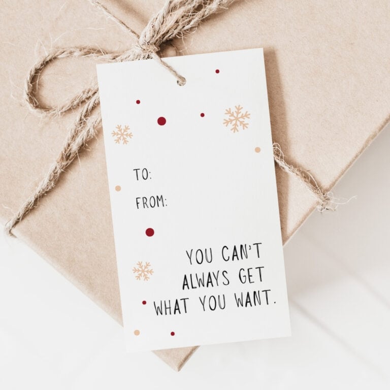 A brown gift box tied with twine features festive Gift Tags reading “TO: FROM:” and below, “YOU CAN’T ALWAYS GET WHAT YOU WANT,” accented with red dots and gold snowflakes.