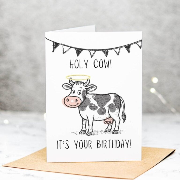 A birthday card featuring a cartoon cow with a yellow halo, black spots, and a banner above it. The card reads, HOLY COW! ITS YOUR BIRTHDAY! and is standing on a brown envelope.