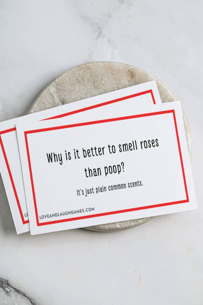 A card featuring one of the best Rose Jokes: “Why is it better to smell roses than poop? It’s just plain common scents.” is placed on a marble surface.